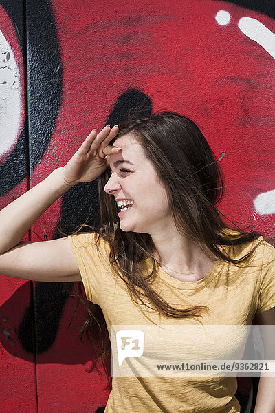 Porträt einer lächelnden jungen Frau  die vor einem Graffiti steht.