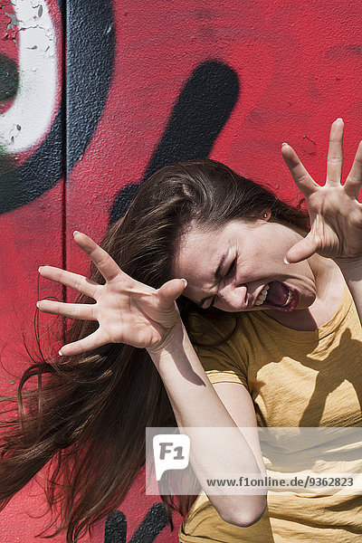 Porträt einer jungen Frau  die vor einem Graffiti ein Gesicht macht