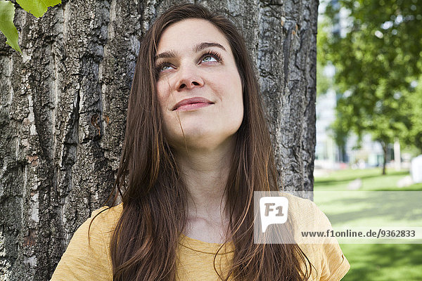 Porträt einer jungen Frau  die vor einem Baumstamm sitzt.