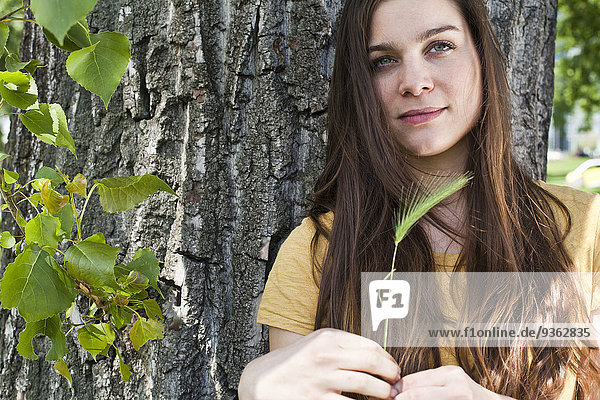 Portrait of young woman with spike in her hand sitting in front of tree trunk