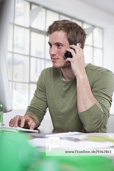 Porträt eines jungen Mannes  der mit seinem Smartphone im Büro telefoniert.