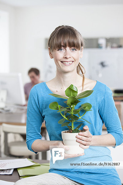Porträt einer lächelnden jungen Frau mit Topfpflanze in einem Kreativbüro