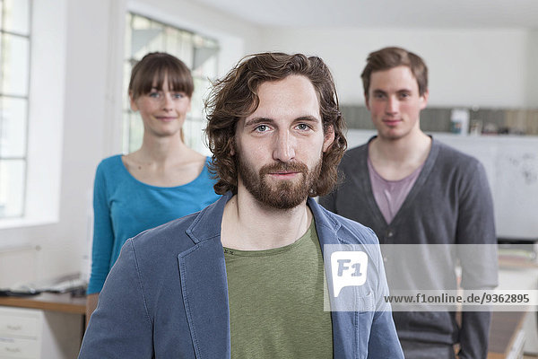 Portrait of young man with his two colleagues in the background standing in a creative office