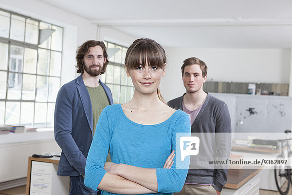 Porträt einer jungen Frau mit ihren beiden Kollegen im Hintergrund in einem Kreativbüro