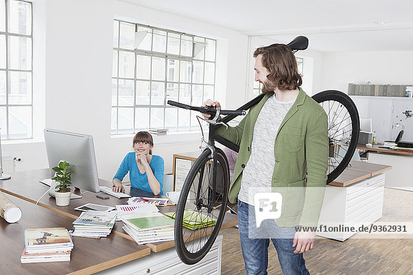 Mann verlässt das Büro mit dem Fahrrad auf der Schulter