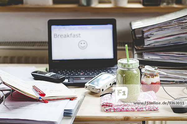 Grüner Smoothie und Joghurt-Frühstück auf dem Schreibtisch mit Laptop
