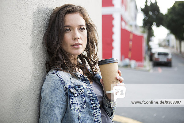 Portrait of young woman with coffee to go leaning at house front