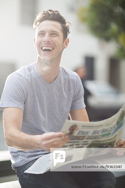 Porträt eines lachenden jungen Mannes mit Zeitung