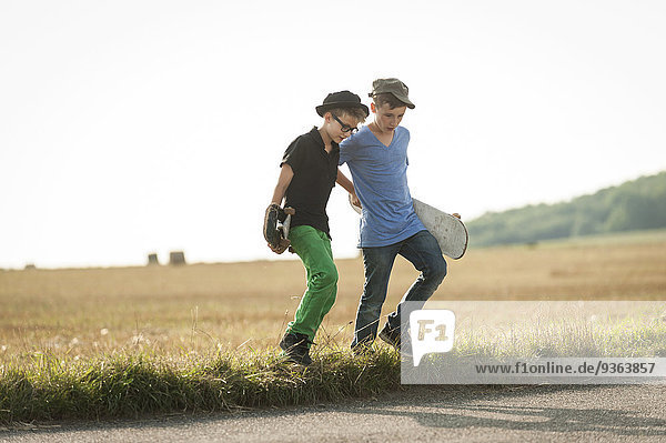 Two boys walking over a field with her skateboards