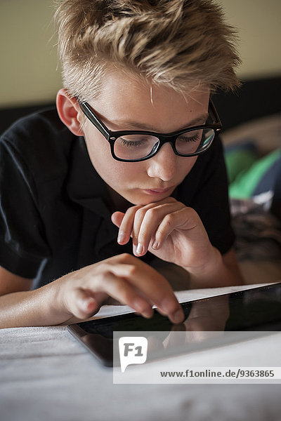 Porträt eines auf dem Bett liegenden Jungen mit digitalem Tablett