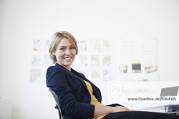 Porträt einer lächelnden jungen Frau an ihrem Schreibtisch in einem Kreativbüro
