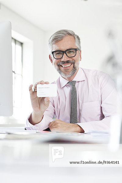 Porträt eines lächelnden Mannes am Schreibtisch mit seiner Visitenkarte