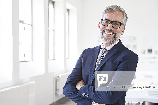 Porträt eines lächelnden Geschäftsmannes mit gekreuzten Armen im Büro