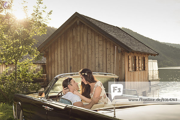 Deutschland  Bayern  Ehepaar im Oldtimer Cabriolet vor der Holzhütte am Schliersee