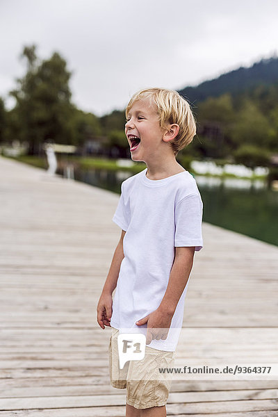 Lachender kleiner Junge auf einem Steg stehend