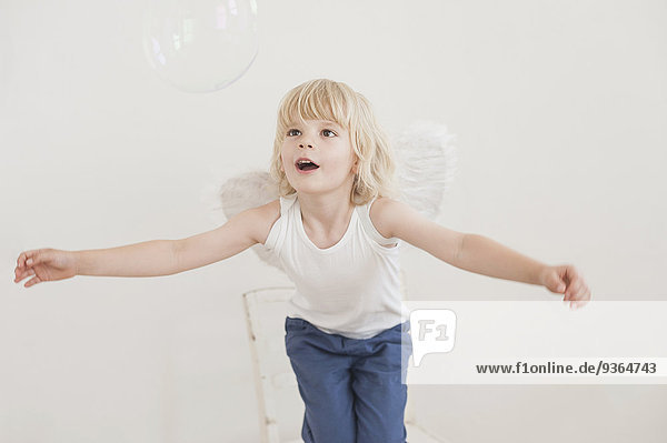 Portrait of gaping little boy with angle wings watching a soap bubble