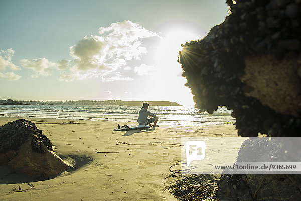 Teenage boy sitting on the beach watching sunset