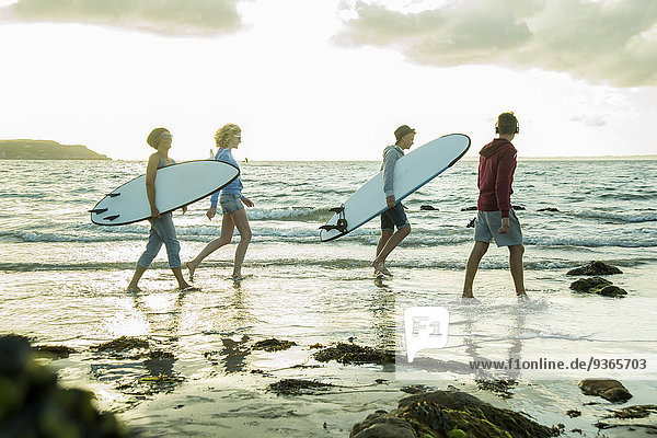 Woman and three teenagers with surfboards walking at waterside of the sea