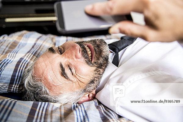Porträt eines lächelnden Geschäftsmannes  der auf seinem Bett liegt und auf sein Smartphone schaut.