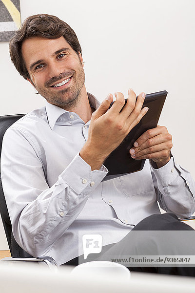 Smiling young businessman with tablet computer in his office