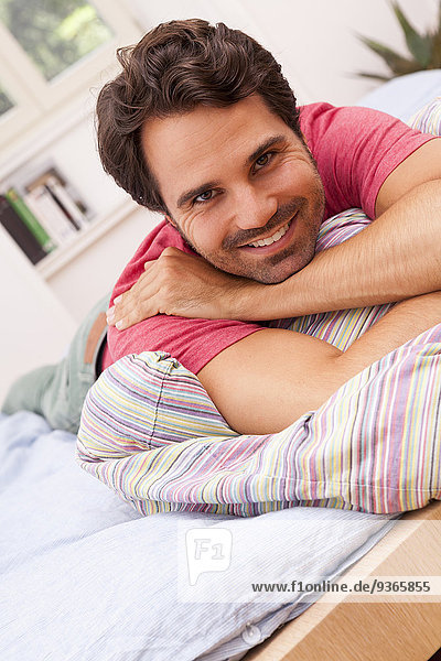 Porträt eines lächelnden jungen Mannes auf dem Bett liegend