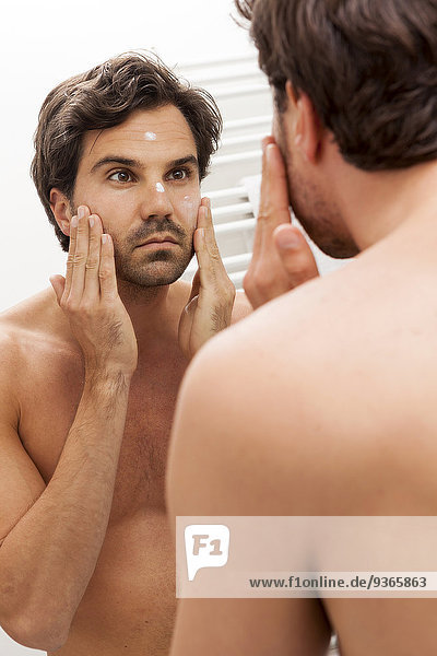 Spiegelbild eines jungen Mannes mit Gesichtscreme