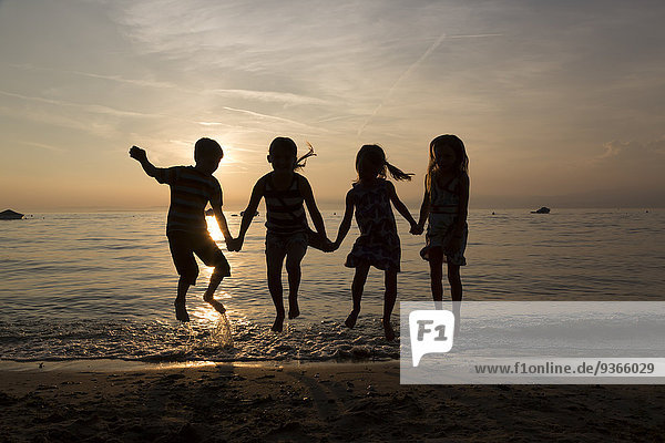 Italien  Gardasee  Kinder springen am Strand bei Sonnenuntergang