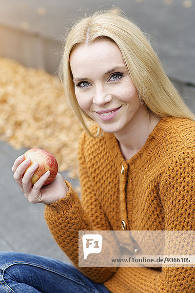 Porträt einer lächelnden jungen Frau mit einem Apfel in Strickjacke