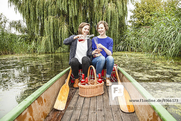 Two young woman in rowing boat with bottle and glass
