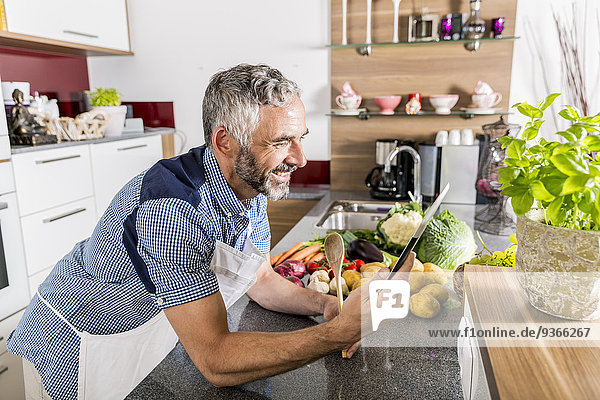Österreich  Mann in der Küche mit digitalem Tablett  sucht Rezept