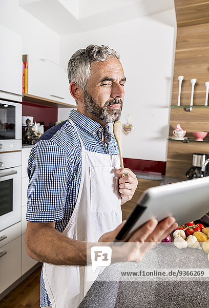 Austria  Man in kitchen holding digital tablet  looking for recipe