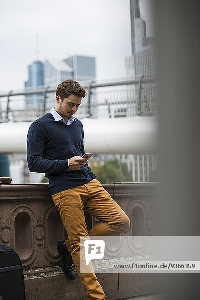 Deutschland  Hessen  Frankfurt  junger Mann auf einer Brücke stehend mit Smartphone