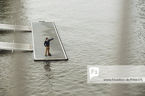 Deutschland  Hessen  Frankfurt  junger Mann  der auf einem Steg steht und mit seinem digitalen Tablett einen Selfie mitnimmt.