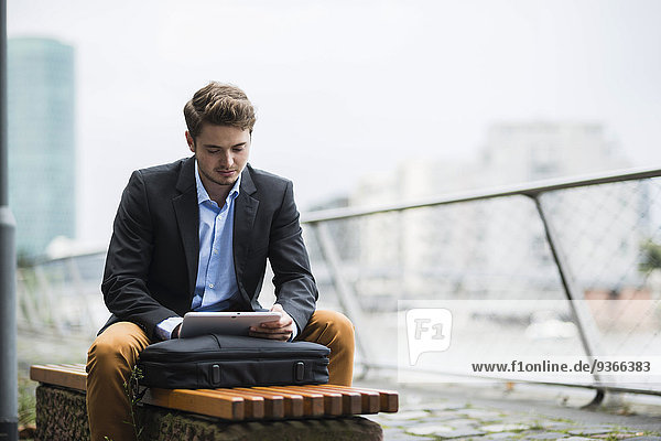 Deutschland  Hessen  Frankfurt  junger Mann auf einer Bank sitzend mit seinem digitalen Tablett