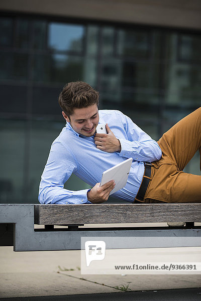 Deutschland  Hessen  Frankfurt  junger Mann auf einer Bank liegend mit seinem digitalen Tablett