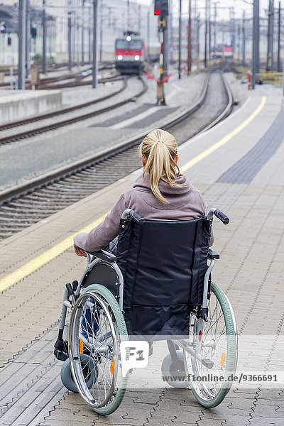 Frau im Rollstuhl am Bahnsteig wartend