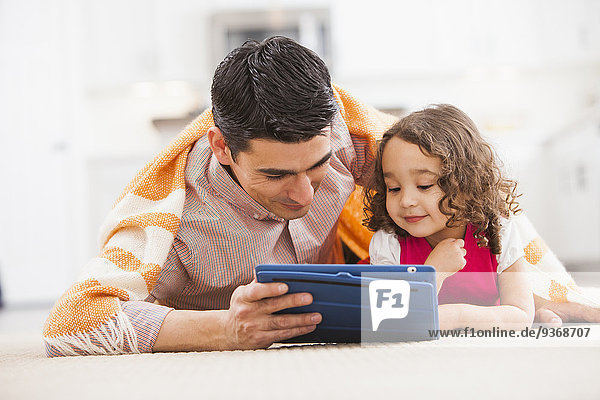 Father and daughter using tablet computer on living room floor