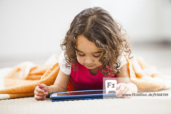 Mixed race girl using tablet computer on living room floor