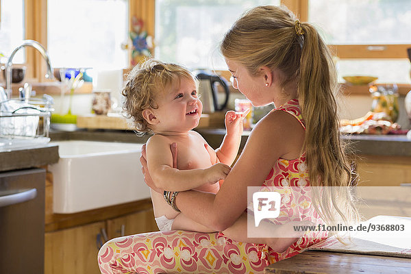 Caucasian girl holding toddler brother in kitchen