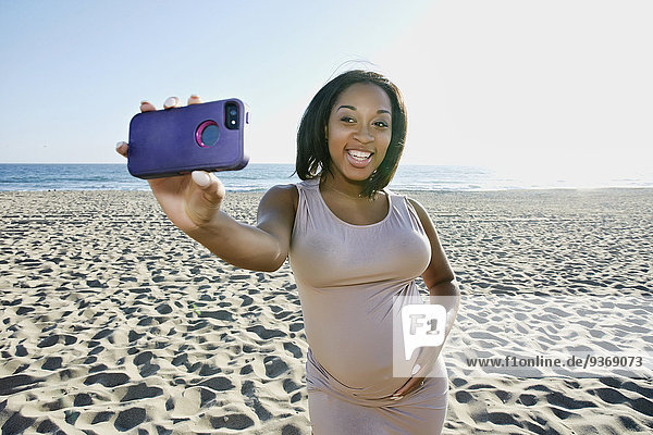Pregnant woman taking cell phone picture on beach