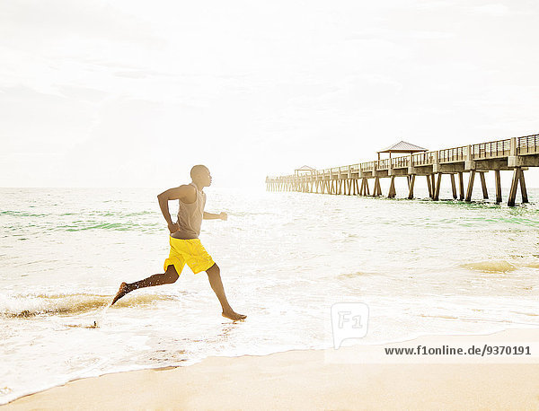 Mixed race barefoot man running on beach