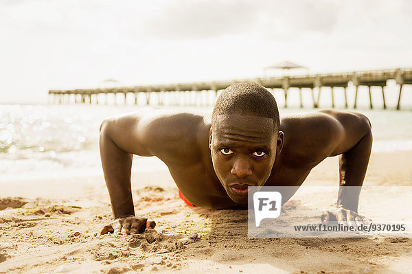 Mixed race man doing push ups on beach