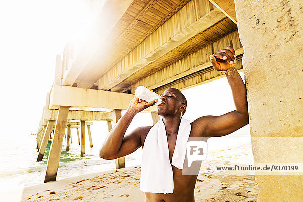 Mixed race man drinking water under pier