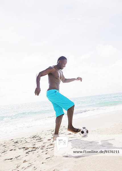 Mixed race man playing with soccer ball on beach