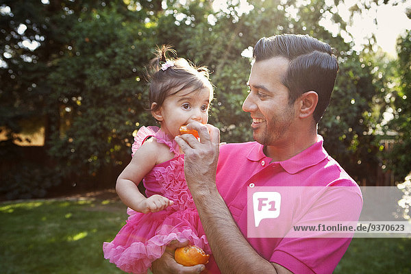 Father feeding daughter orange outdoors