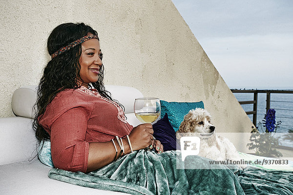 Mixed race woman drinking wine at waterfront with dog