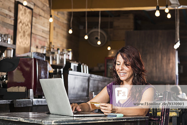 Hispanic woman shopping on laptop in coffee shop