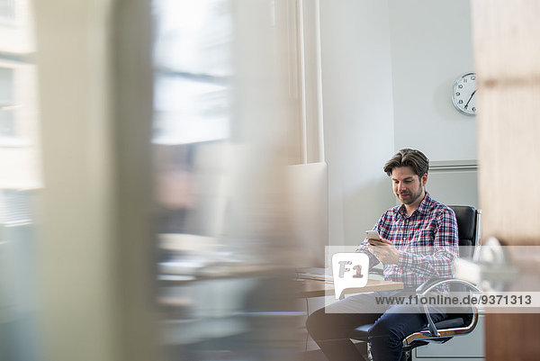 Blick durch eine Bürotrennwand eines am Schreibtisch sitzenden Mannes.