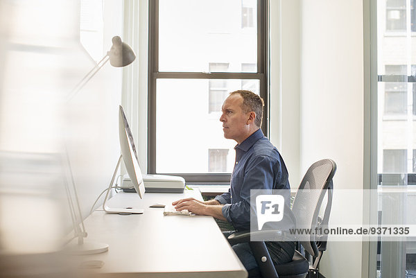 Ein Geschäftsmann  der an seinem Schreibtisch sitzt und an einem Computer arbeitet.