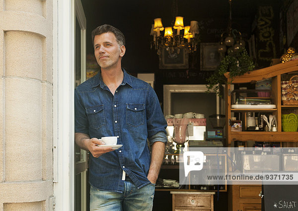 Mann steht in Ladeneingang  mit Kaffeetasse